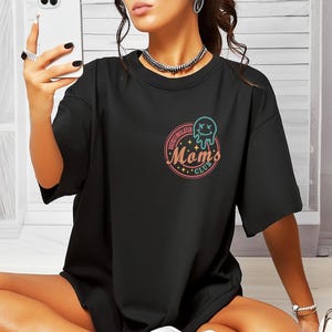 May include: Black oversized t-shirt with a graphic of a dripping smiley face and the text "Over-Stimulated Moms Club".