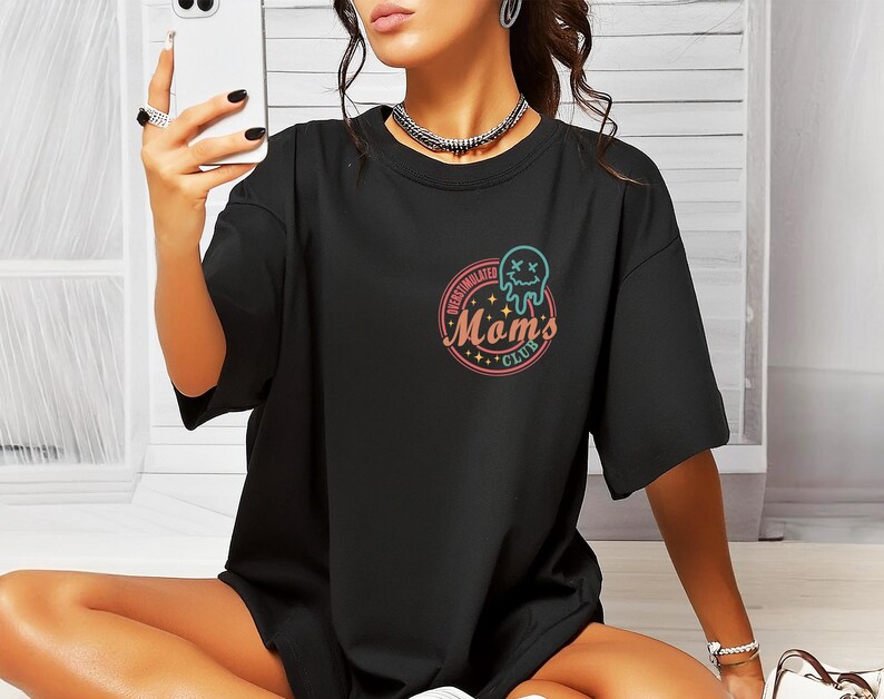 May include: Black oversized t-shirt with a graphic of a dripping smiley face and the text "Over-Stimulated Moms Club".