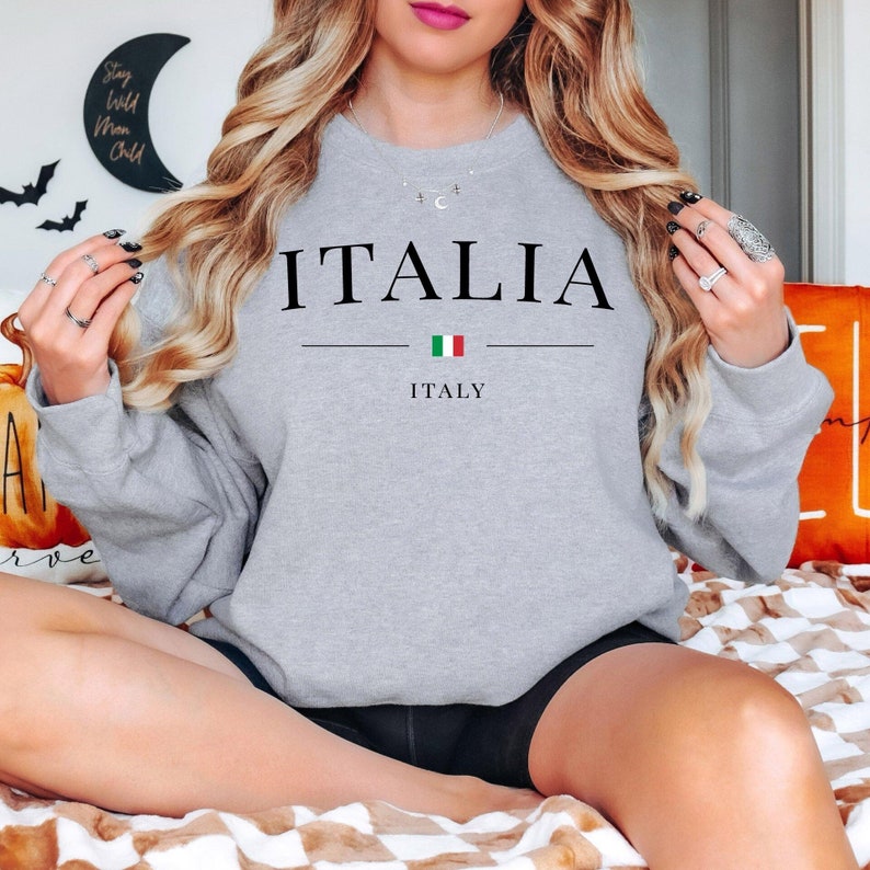May include: A light gray sweatshirt with the word "ITALIA" printed in black. Below the word is a horizontal line, the Italian flag, and the word "ITALY". The sweatshirt is a crew neck style.
