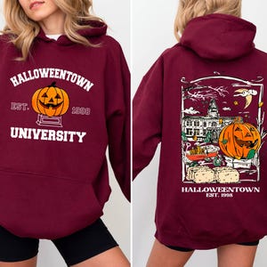 May include: Burgundy hooded sweatshirt with "Halloweentown University" text and a jack-o'-lantern graphic on the front. The back features a detailed Halloween-themed illustration with a pumpkin, buildings, and the text "Halloweentown Est. 1998".