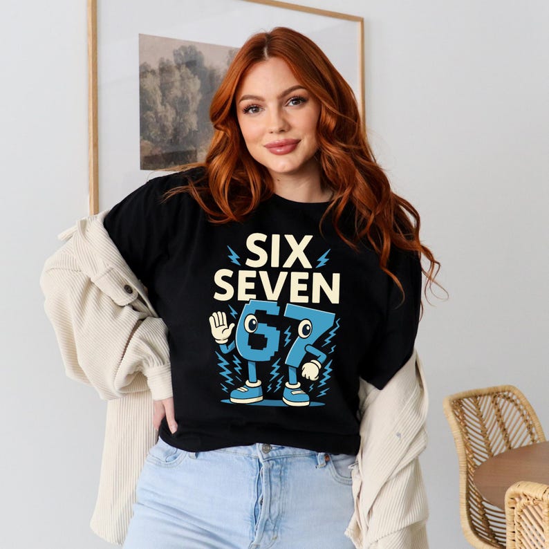 May include: Black t-shirt with the words "SIX SEVEN" in a bold, retro font. The numbers "6" and "7" are designed as cartoon characters in blue, with arms, legs, and shoes. The shirt is worn by a person.