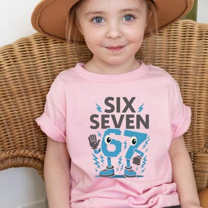 May include: A pink t-shirt with the words "SIX SEVEN" and the number "67" in a cartoon style. The number has eyes, arms, and legs. The shirt is worn by a young child.