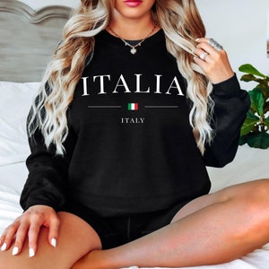 May include: Black sweatshirt with the word "ITALIA" in white capital letters. Below the word is a horizontal line, the Italian flag, and the word "ITALY". The sweatshirt is a crew neck style.