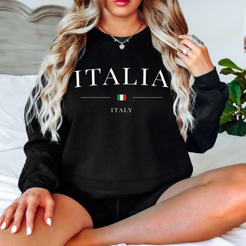 May include: Black sweatshirt with the word "ITALIA" in white capital letters. Below the word is a horizontal line, the Italian flag, and the word "ITALY". The sweatshirt is a crew neck style.