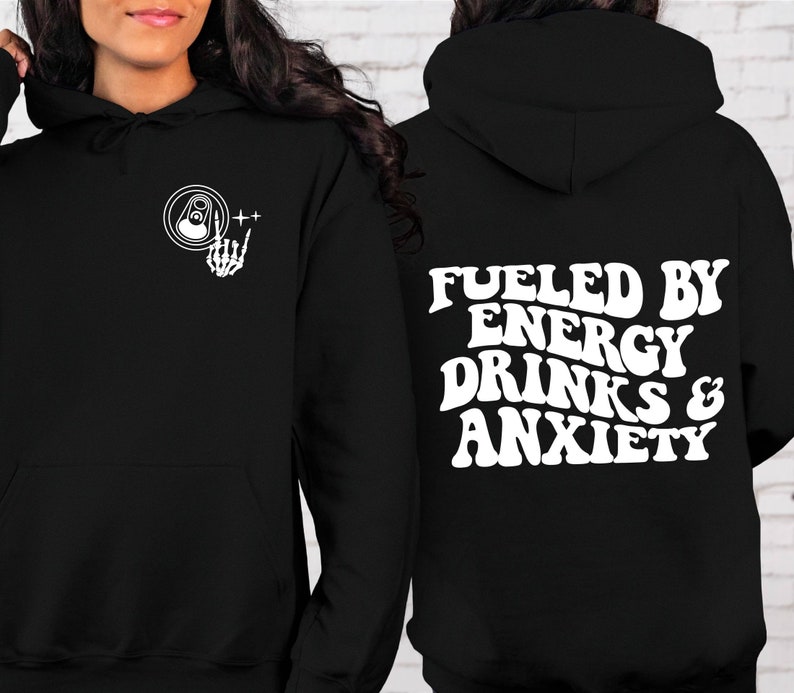 Puede incluir: Sudadera con capucha negra con un gr&aacute;fico blanco de una lata y una mano de esqueleto en la parte delantera y el texto "Fueled by Energy Drinks & Anxiety" en la parte posterior.