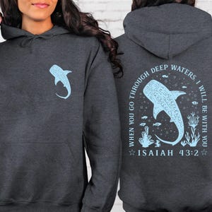 May include: Dark gray hoodie with a light blue whale shark graphic on the front and back. The back features the text "WHEN YOU GO THROUGH DEEP WATERS, I WILL BE WITH YOU" and "ISAIAH 43:2". The hoodie has a drawstring hood and a front pocket.