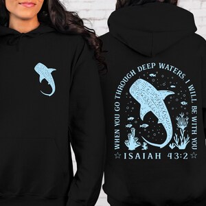 May include: Black hoodie with a light blue whale shark graphic on the front and back. The back design includes the text "WHEN YOU GO THROUGH DEEP WATERS, I WILL BE WITH YOU" and "ISAIAH 43:2". The hoodie has a drawstring hood and a kangaroo pocket.
