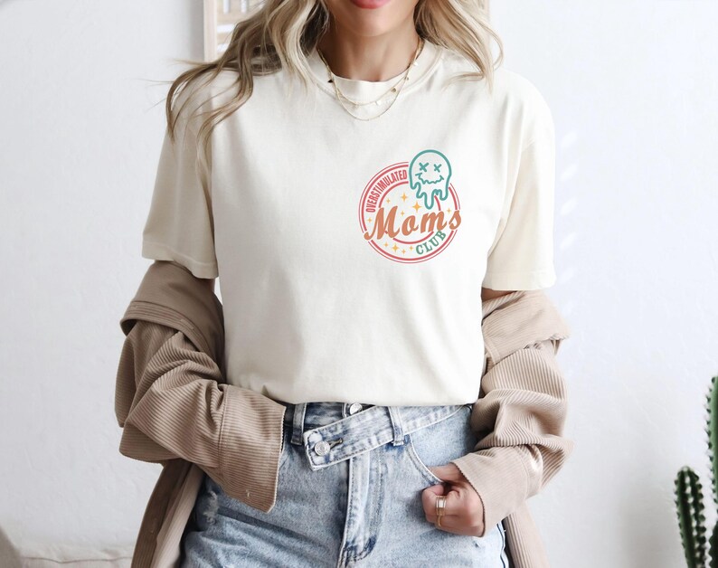 May include: A white t-shirt with a graphic of a melting ice cream cone with a face and the text "Overstimulated Moms Club".