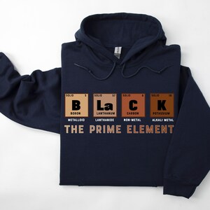 Puede incluir: Sudadera con capucha azul marino con un gr&aacute;fico de la palabra "BLACK" deletreada usando los s&iacute;mbolos qu&iacute;micos de boro, lantano, carbono y potasio. El texto "THE PRIME ELEMENT" est&aacute; impreso debajo del gr&aacute;fico.