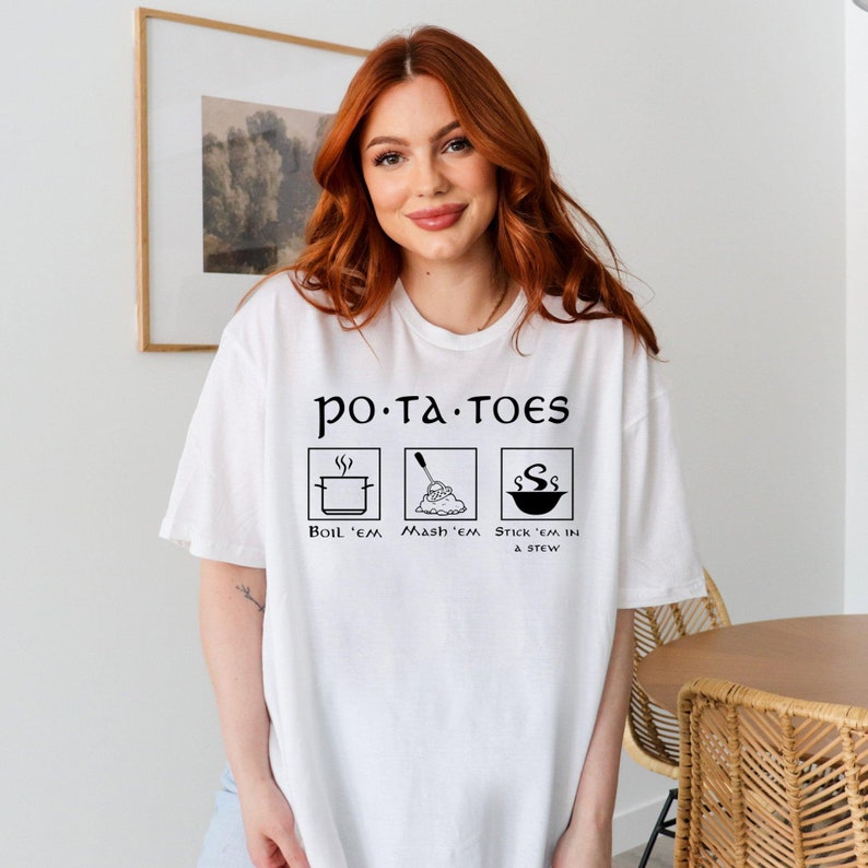 May include: White t-shirt with a black graphic that says "po-ta-toes" and shows three ways to prepare potatoes: boil, mash, and stick in a stew.