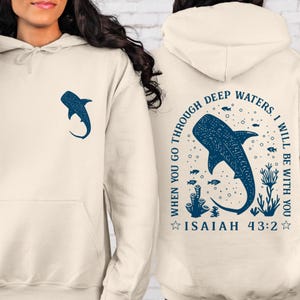 May include: Cream-colored hoodie with a blue whale shark graphic on the front and back. The back design includes the text "When you go through deep waters, I will be with you. Isaiah 43:2."