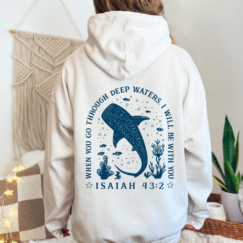 May include: White hoodie with a blue graphic of a whale shark, fish, and coral. Text in a circular design reads "When you go through deep waters, I will be with you. Isaiah 43:2."