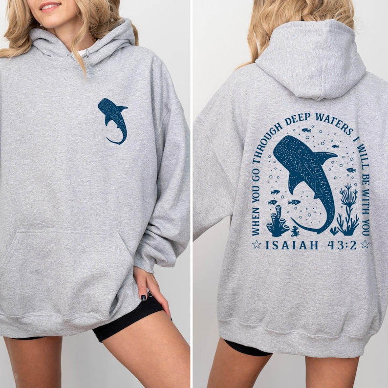 May include: A light gray hoodie with a front pocket and a hood. The front features a dark blue whale shark graphic. The back of the hoodie has a larger whale shark design with the text "WHEN YOU GO THROUGH DEEP WATERS, I WILL BE WITH YOU" and "ISAIAH 43:2".