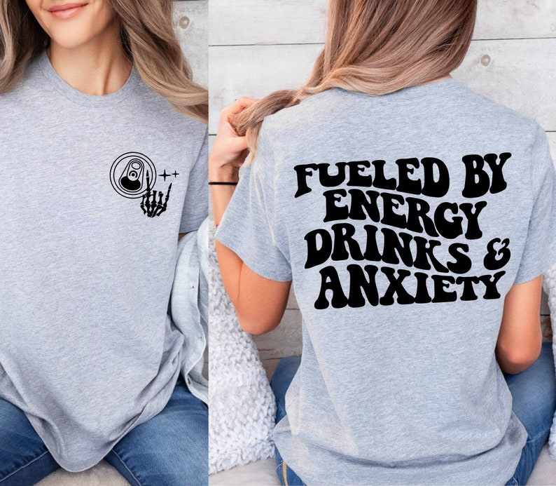 May include: Gray t-shirt with a black graphic on the front of a can with a skeleton hand giving the rock and roll sign. The back of the shirt has the text "Fueled by Energy Drinks & Anxiety" in black.