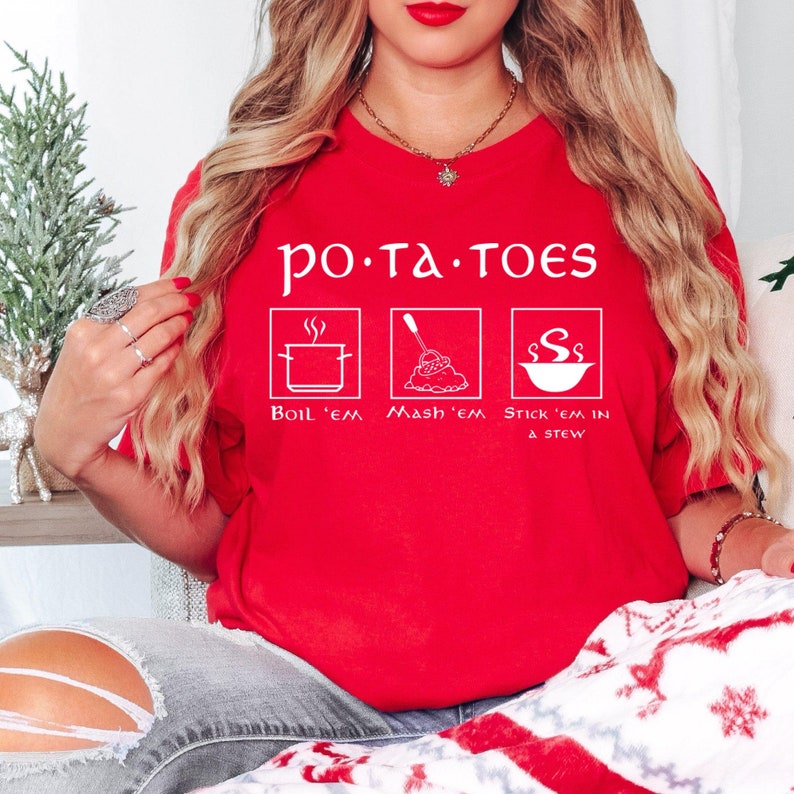 May include: Red t-shirt with white text that reads "po.ta.toes" and three illustrations of potatoes being prepared: boiled, mashed, and in a stew. The text below the illustrations reads "Boil 'em Mash 'em Stick 'em in a stew."