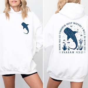 May include: White hoodie with a blue whale shark graphic on the front and back. The back graphic includes the text "WHEN YOU GO THROUGH DEEP WATERS, I WILL BE WITH YOU" and "ISAIAH 43:2". The hoodie has a drawstring hood and a front pocket.