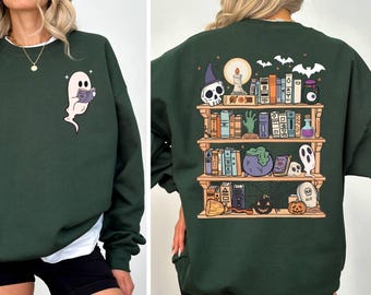 May include: A dark green sweatshirt with a graphic of a bookshelf filled with spooky Halloween items, including books, a cauldron, a skull, and a ghost. The text "RIP" is visible on the graphic.