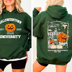 May include: Dark green Halloween-themed hoodie with a front graphic of a jack-o'-lantern and the text "Halloweentown University Est. 1998." The back features a detailed illustration of a pumpkin, a building, and the text "Halloweentown Est. 1998."