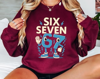 May include: Burgundy sweatshirt with the text "SIX SEVEN" in cream-colored letters and a cartoon graphic of the numbers 6 and 7. The numbers are blue with white accents and lightning bolt details.