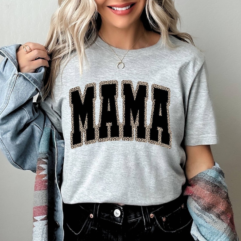 Może przedstawiać: Szary T-shirt z czarnym nadrukiem "MAMA". Litery są obwiedzione wzorem w panterkę.