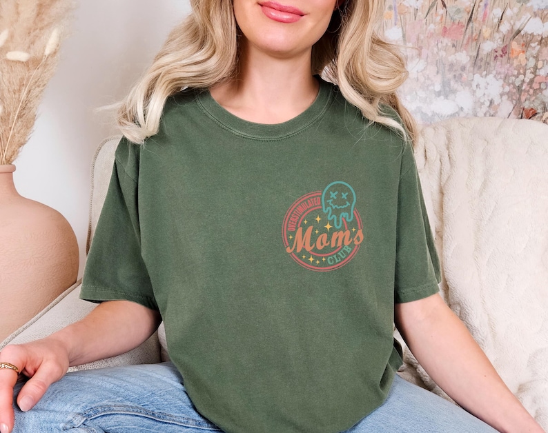 May include: A green t-shirt with a retro-style graphic that says "Spelling Bee Mom's Club" with a cartoon ghost wearing a crown.