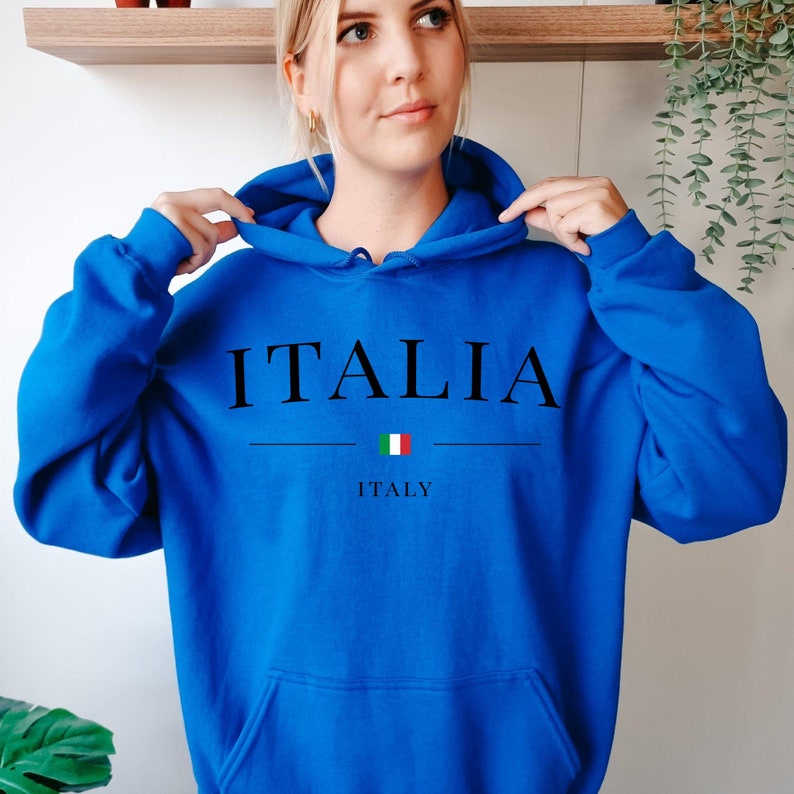 May include: A royal blue hoodie with the word "ITALIA" in black capital letters. Below the word is a horizontal line, and beneath that is the Italian flag and the word "ITALY". The hoodie has a hood and a front pocket.