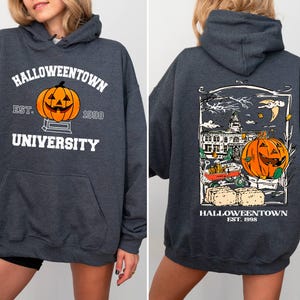 May include: Dark gray hooded sweatshirt with "Halloweentown University" and a jack-o'-lantern graphic on the front. The back features a detailed Halloween scene with a pumpkin, buildings, and the text "Halloweentown Est. 1998".