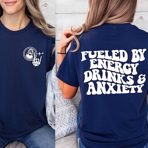 May include: A navy blue t-shirt with a white graphic on the front of a can with a skeleton hand giving a rock and roll sign. The back of the shirt has white text that reads "Fueled by Energy Drinks & Anxiety".