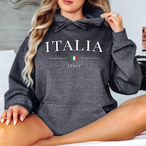 May include: Dark gray hoodie with the word "ITALIA" in white capital letters. Below the word is a horizontal line, the Italian flag, and the word "ITALY". The hoodie has a drawstring hood and a front pocket.