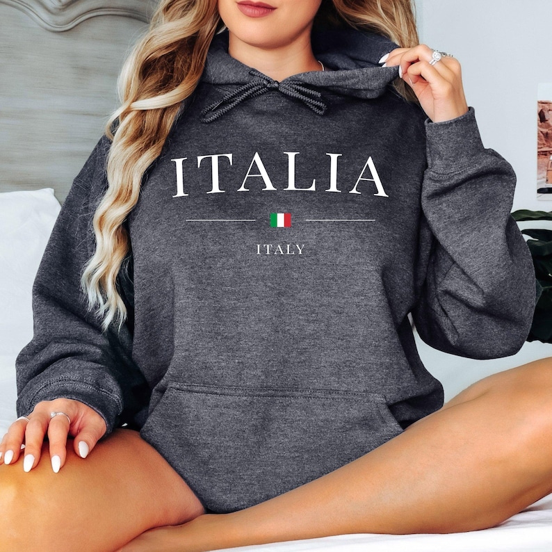 May include: Dark gray hoodie with the word "ITALIA" in white capital letters. Below the word is a horizontal line, the Italian flag, and the word "ITALY". The hoodie has a drawstring hood and a front pocket.