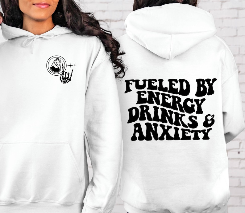Puede incluir: Sudadera con capucha blanca con un gr&aacute;fico negro en la parte delantera de una lata con una mano de esqueleto haciendo el signo de rock and roll. La parte posterior de la sudadera tiene el texto "Fueled by Energy Drinks & Anxiety" en una fuente retro.