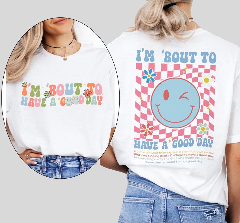 May include: White t-shirt with the text "I'M 'BOUT TO HAVE A GOOD DAY" in colorful, retro-style lettering. The back features a smiley face, flowers, and a checkered pattern. The shirt has a relaxed fit.