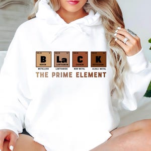 Puede incluir: Sudadera blanca con un gr&aacute;fico de la tabla peri&oacute;dica de los elementos que deletrea "BLACK" con las palabras "The Prime Element" debajo. Los elementos son B, La, C y K, que representan Boro, Lantano, Carbono y Potasio.