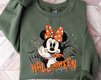 May include: Green sweatshirt featuring a Halloween-themed Minnie Mouse graphic. Minnie Mouse is wearing an orange polka-dot bow and holding a pumpkin. The word "HALLOWEEN" is printed in orange, with bats and a spooky tree in the background.