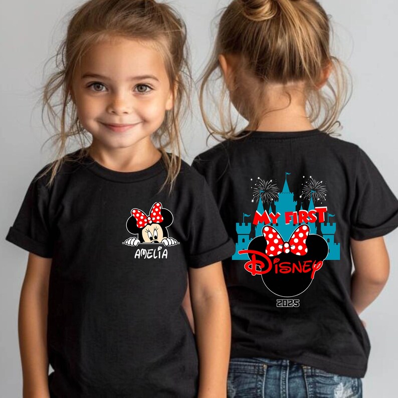 May include: Black t-shirts featuring a Minnie Mouse design. The front of the shirt has a Minnie Mouse graphic with a red bow and the name "Amelia". The back of the shirt has a castle graphic, fireworks, and the words "My First Disney" and "2025".