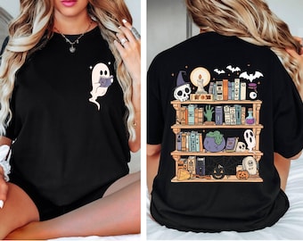 May include: Black t-shirt featuring a ghost reading a book on the front and a spooky bookshelf design on the back. The bookshelf includes books, a skull, a cauldron, and other Halloween-themed elements. The design is in shades of orange, purple, and green.
