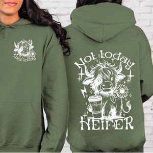 Może przedstawiać: Zielona bluza z kapturem z białym nadrukiem przedstawiającym krowę szkocką trzymającą kubek kawy i tekstem "Not today Heifer".