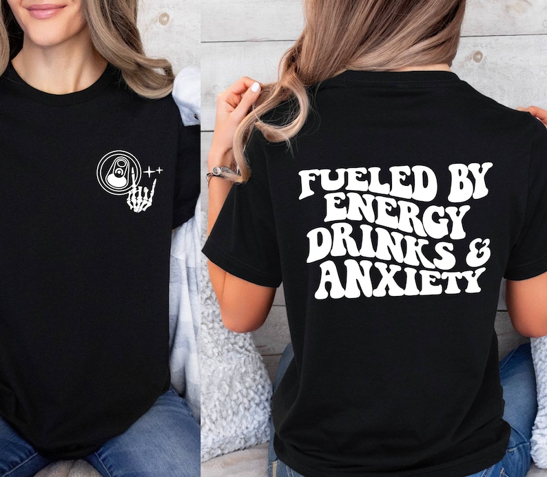 May include: Black t-shirt with white text that reads "Fueled by Energy Drinks & Anxiety". The front of the shirt has a white graphic of a skeleton hand holding a can.