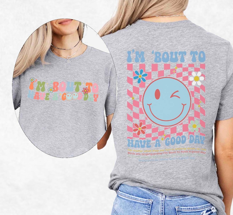 May include: A light gray t-shirt with the text "I'M BOUT TO HAVE A GOOD DAY" in colorful, retro-style lettering. The back of the shirt features a smiley face and a checkered pattern.