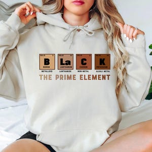 Puede incluir: Una sudadera con capucha blanca con un estampado gr&aacute;fico de las letras "BLaCK" que representan los elementos qu&iacute;micos Boro, Lantano, Carbono y Potasio. El texto "THE PRIME ELEMENT" est&aacute; impreso debajo del gr&aacute;fico.