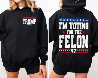 Peut inclure: Sweat-shirt à capuche noir avec un motif blanc sur le devant qui dit "TRUMP 2024" et un motif blanc sur le dos qui dit "I'M VOTING FOR THE FELON 47" avec des étoiles rouges et bleues.