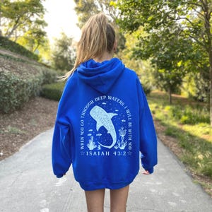 May include: A royal blue hoodie with a white graphic on the back. The graphic features a whale shark, aquatic plants, and the text "WHEN YOU GO THROUGH DEEP WATERS, I WILL BE WITH YOU. ISAIAH 43:2."