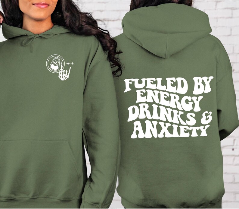 Puede incluir: Una sudadera con capucha verde con el texto "Fueled by Energy Drinks & Anxiety" en blanco en la espalda. La parte delantera de la sudadera tiene un gr&aacute;fico blanco de una lata con una mano de esqueleto haciendo el signo de rock and roll.