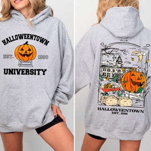 May include: A light gray Halloween-themed hoodie with a front graphic of a jack-o'-lantern and the text "Halloweentown University Est. 1998." The back features a larger graphic with a pumpkin, buildings, and the text "Halloweentown Est. 1998."