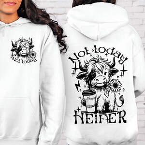 Może przedstawiać: Biała bluza z kapturem z czarno-białym rysunkiem krowy trzymającej kubek kawy i słonecznik. Na plecach bluzy nadrukowany jest napis "Not today heifer".