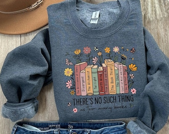 May include: A dark gray sweatshirt with a floral and book graphic. The graphic includes book titles like "Divergent" and "Twilight", with the text "THERE'S NO SUCH THING as too many books". A brown hat and blue jeans are also visible.