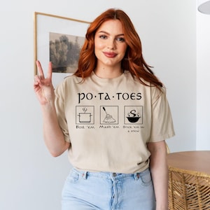 May include: A beige t-shirt with a graphic of a potato with the text "po.ta.toes" and three icons showing different ways to prepare potatoes: "boil 'em", "mash 'em", and "stick 'em in a stew".