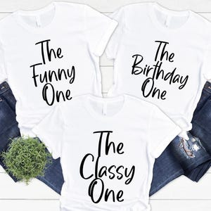 Peut inclure: Trois t-shirts blancs avec du texte noir. Les t-shirts disent "The Funny One", "The Birthday One", et "The Classy One".