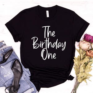 Peut inclure: T-shirt noir avec du texte blanc qui dit "The Birthday One".