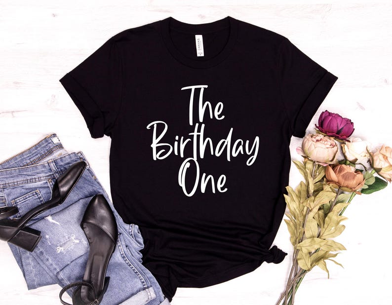 Peut inclure: T-shirt noir avec du texte blanc qui dit "The Birthday One".
